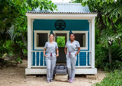 dr. tracey and jesica standing outside a cayman house in their mobile vet uniforms